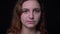 Close-up shot of young wavy-haired student watching seriously and attentively into camera at black background.