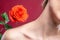 Close-up shoulder neck and collarbone of attractive young girl on red background next to red rose
