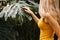 Close-up side portrait of a blonde woman in a yellow bathing suit on a background of exotic woods and the leaves of the monstera