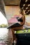 Close-up side view of attractive woman in swimsuit and with wakeboard sit on edge of boat under bridge