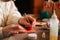 Close-up side view hands of young woman writing number on red bag by brush and white paint sitting at table.