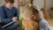 Close-up side view of little pretty girl hugging teddy bear with blurred boys talking at background. Portrait of