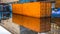Close up side view of orange shipping container reflecting in pu