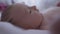 Close-up side view portrait curios infant lying in bed looking around moving hands. Caucasian newborn baby girl at home