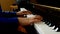 Close up side view of young hands and fingers playing a song on the keys of an upright shiny black piano.