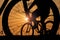 Close-up silhouette of a bike wheel at sunset. The sun shines through the wheel of a bicycle with blurred silhouette of bicycle ri