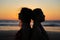 Close up silhouette of womens couple in romantic scene of sunset over the sea. Beautiful female young lesbian couple in love