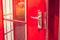 Close up silver metal door handle on opened red modern door of phone booth.