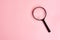 Close up Single Magnifying Glass with Black Handle, Leaning on pink background