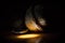 Close up of a single walnut next to remains of a cracked shell in a small bright spotlight and darkness all around