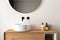 Close up of sink with oval mirror standing in on white wall , wooden cabinet with black faucet in minimalist bathroom. Side view.