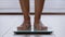 Close-up slender female legs unrecognizable woman standing barefoot in bathroom stepping on electronic scales checking