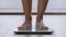 Close-up slender female legs unrecognizable woman walking barefoot across room stepping on electronic scales checking