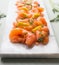 Close up of slices of homemade smoked salmon with dill and lemon served on marble cutting board on light background. Top view.