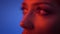 Close-up slide shot in profile of fashion model face watching seriously upwards in red neon light on blue background.