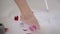 Close-up slim female foot touching bath foam with rose petals. Unrecognizable young slender Caucasian woman checking