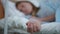 Close-up slim female hand on hospital bed indoors with blurred teenage girl lying at background. Unrecognizable sick