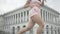 Close-up of slim female legs dancing twerk in city center. Positive young Caucasian woman in pink clothes turning to