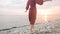 Close-up slow motion following behind the legs of a barefoot girl in a red dress fluttering in the wind at sunset