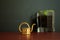 Close up of a small golden watering can tool and a glass filled with basil in the background.