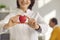 Close up of a small red heart that is held in the hands of a smiling female cardiologist.