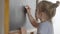 Close-up of smart cute Caucasian girl writing math problem on chalkboard. Bright intelligent pupil learning studying in