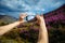 Close-up of smartphone in hands. Unknown woman using a gadget takes photos of a mountain slope covered with pink flowers