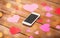 Close up of smartphone and hearts on wood
