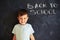 Close-up of smiling cute schoolboy near blackboard in class