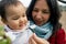 close up of smiling mother and baby daughter picking up cherry flowers during blossom season in spring. concept of motherhood and