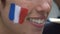 Close up of smiling woman face painting flag of France on cheeks, make-up