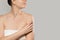 Close up of smiling woman touching soft skin on shoulder over grey background. Beauty procedure  body cream advertisement concept.