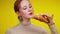 Close-up of smiling young freckled redhead woman showing tray with pastry and tasting sweet delicious croissant