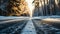Close-up of a snow covered empty rural asphalt road through a dense conifer forest at sunset
