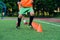 Close up soccer player`s legs running among plastic orange cones that standing on artificial stadium during workout.