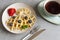 Close-up of soft Viennese waffles on the plate with blueberries, strawberry, chocolate sauce and cup of tea