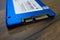 Close-up: A solid-state drive of bright blue color lies on the surface with a wooden texture. Macro photo of SATA connector