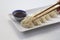 Close-up of some Asian jiaozis or gyozas on a white ceramic plate and a blue ceramic bowl with soy sauce and sesame seeds on white