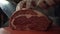 Close-up of somebody`s hands in protective gloves neatly chopping the meat on the cutting board. Action. Cutting meat