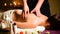 Close-up spa massage woman`s shoulders and back. Male hands do massage to a woman in a dark room with candles in the