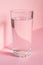 Close up of sparkling water in transparent high glass and sun glare on pink background