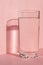 Close up of sparkling water in transparent high glass and sun glare on pink background