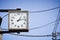 Close up of square vintage analog clock on black metal post with blue sky and electric wires background, copy space