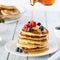 Close up of a stack of buttermilk pancakes with maple syrup being poured on top.