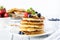 Close up of a stack of buttermilk pancakes topped with berries, banana and syrup and garnished with mint.