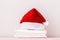 Close-up of a stack of clean white bedding and a Santa hat, on a table against a light wall. Copy space