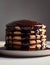 Close-up of a stack of fluffy pancakes drizzled with chocolate sauce on a plate against a gray background. Morning sweet