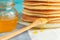 Close up of stack of pancake with pouring honey, wooden spoon and jar of honey