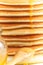Close up of stack of pancake with pouring honey, wooden spoon and jar of honey