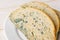 Close-up of stale bread with green mildew on a white saucer over white wooden table. Spoiled bread with mold. Moldy fungus on